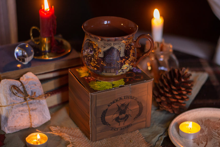 Persimmon orange heat-sealed 360Â° printed mug of a witchâ€™s cottage,  featuring a warm autumnal design with a sleeping kitten, pumpkins, leaves, and a vintage arched doorway scene, placed on a cozy table. Harvest drying out for winter and much more. Microwave and dishwasher safe. They are a rounded shape with a wide lip, to keep your hands cozy all winter long. 