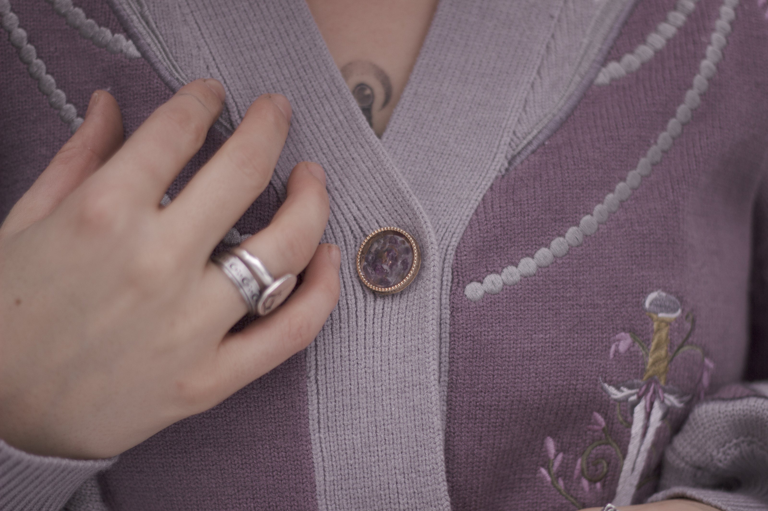 A soft button-up lavender and light plum knit cardigan shown in two styles: cropped and full-length. The design features intricate embroidery of swords and silver armour accents, evoking a medieval and fantasy-inspired look.
