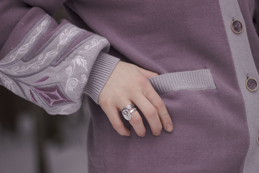 A soft button-up lavender and light plum knit cardigan shown in two styles: cropped and full-length. The design features intricate embroidery of swords and silver armour accents, evoking a medieval and fantasy-inspired look.