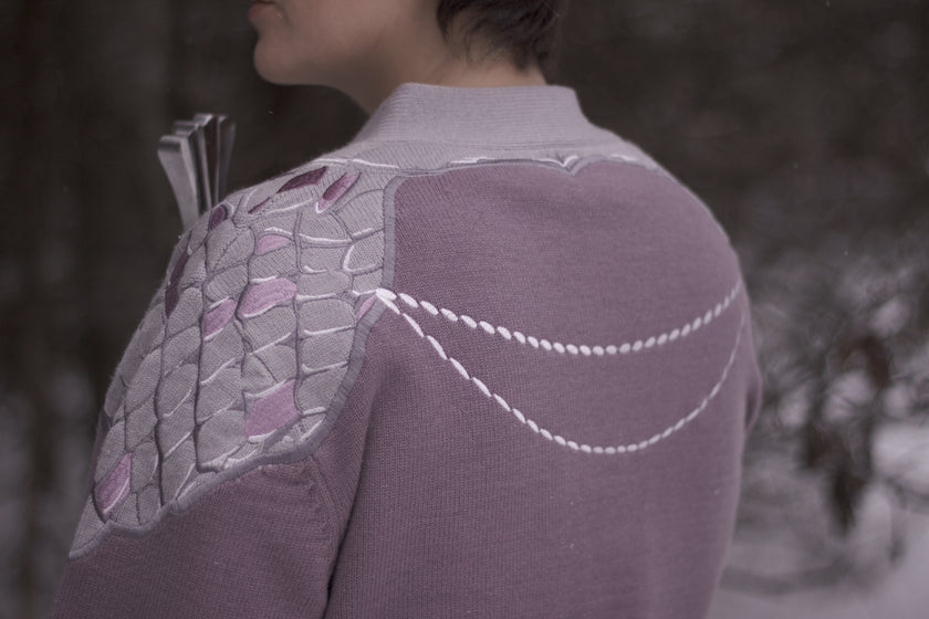 A soft button-up lavender and light plum knit cardigan shown in two styles: cropped and full-length. The design features intricate embroidery of swords and silver armour accents, evoking a medieval and fantasy-inspired look.