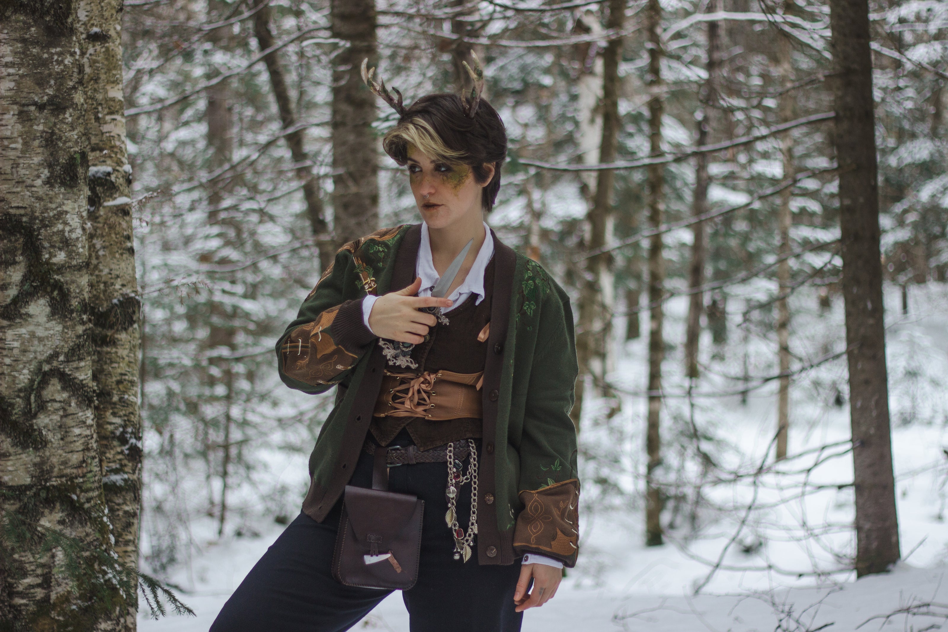  A soft button-up chestnut-brown and forest-green knit cardigan. The design features intricate embroidery of english ivy, dagger, and sturdy armour, evoking a whimsical and fantasy-inspired look.