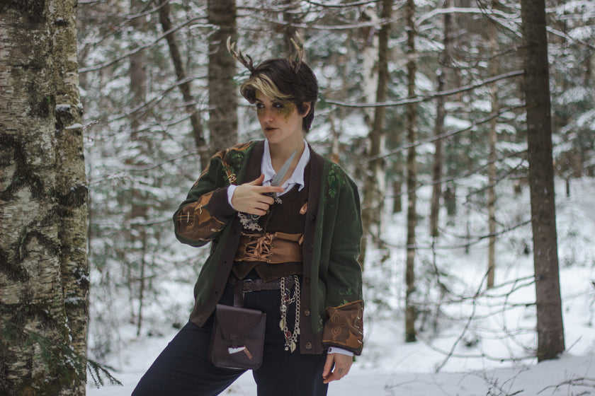  A soft button-up chestnut-brown and forest-green knit cardigan. The design features intricate embroidery of english ivy, dagger, and sturdy armour, evoking a whimsical and fantasy-inspired look.