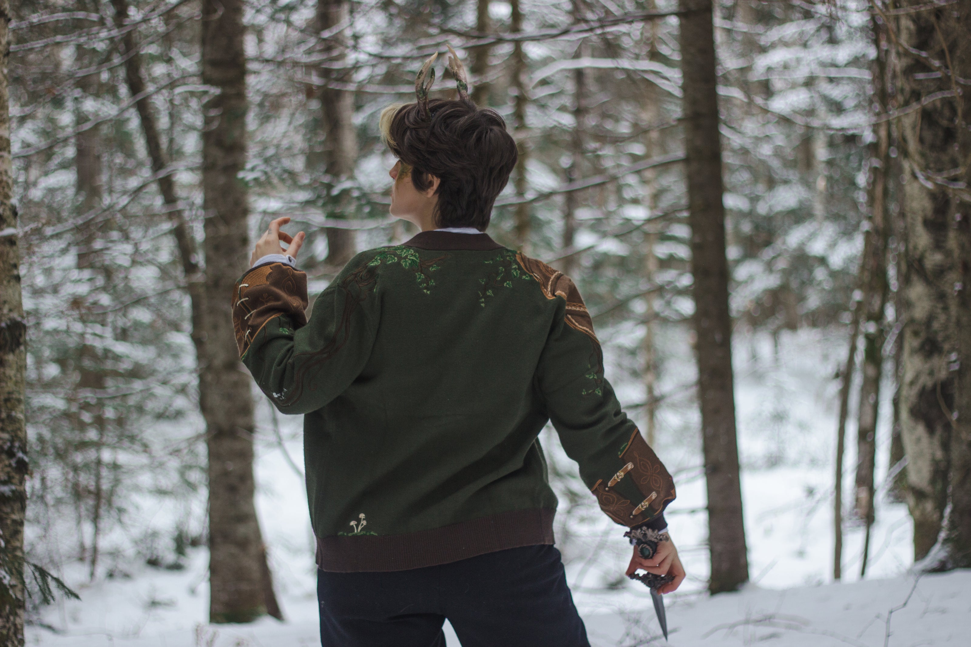 A soft button-up chestnut-brown and forest-green knit cardigan. The design features intricate embroidery of english ivy, dagger, and sturdy armour, evoking a whimsical and fantasy-inspired look.