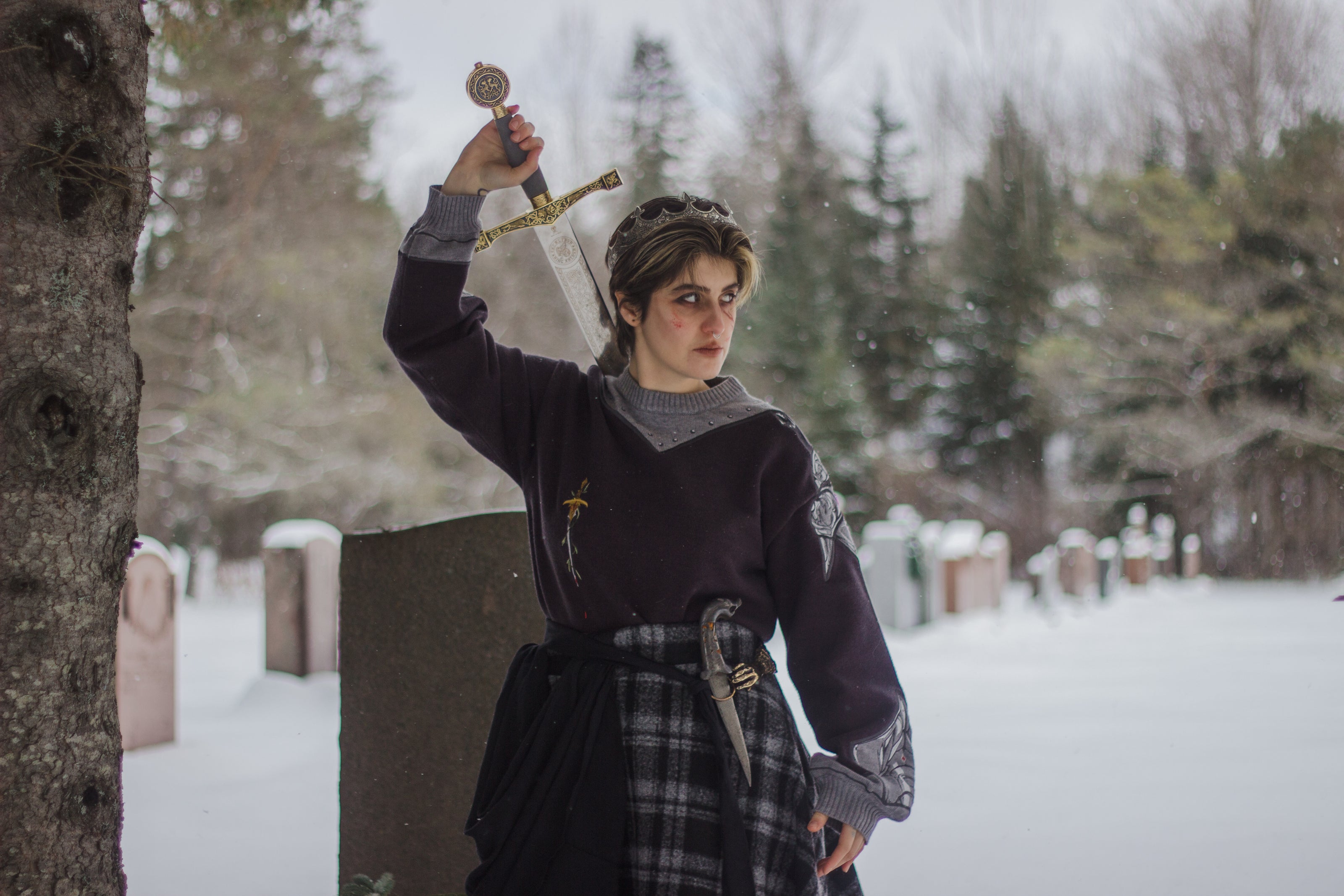A soft, dark purple with a slight brown undertone and silver knit crewneck sweater, with red embellishments. The design features intricate embroidery of a vine wrapped sword and sturdy armour. Evoking a whimsical and fantasy-inspired look.