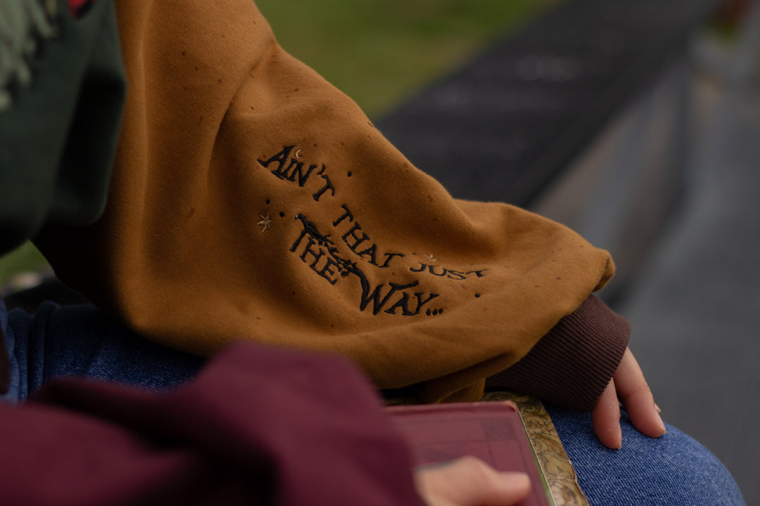 Cozy, oversized, puff-sleeved, color-blocked, cotton crewneck sweater in forest green, with burgundy, and mustard coloured sleeves. The sweater features an intricately embroidered design of a green frog with a red wizard hat and a red lantern on the chest.