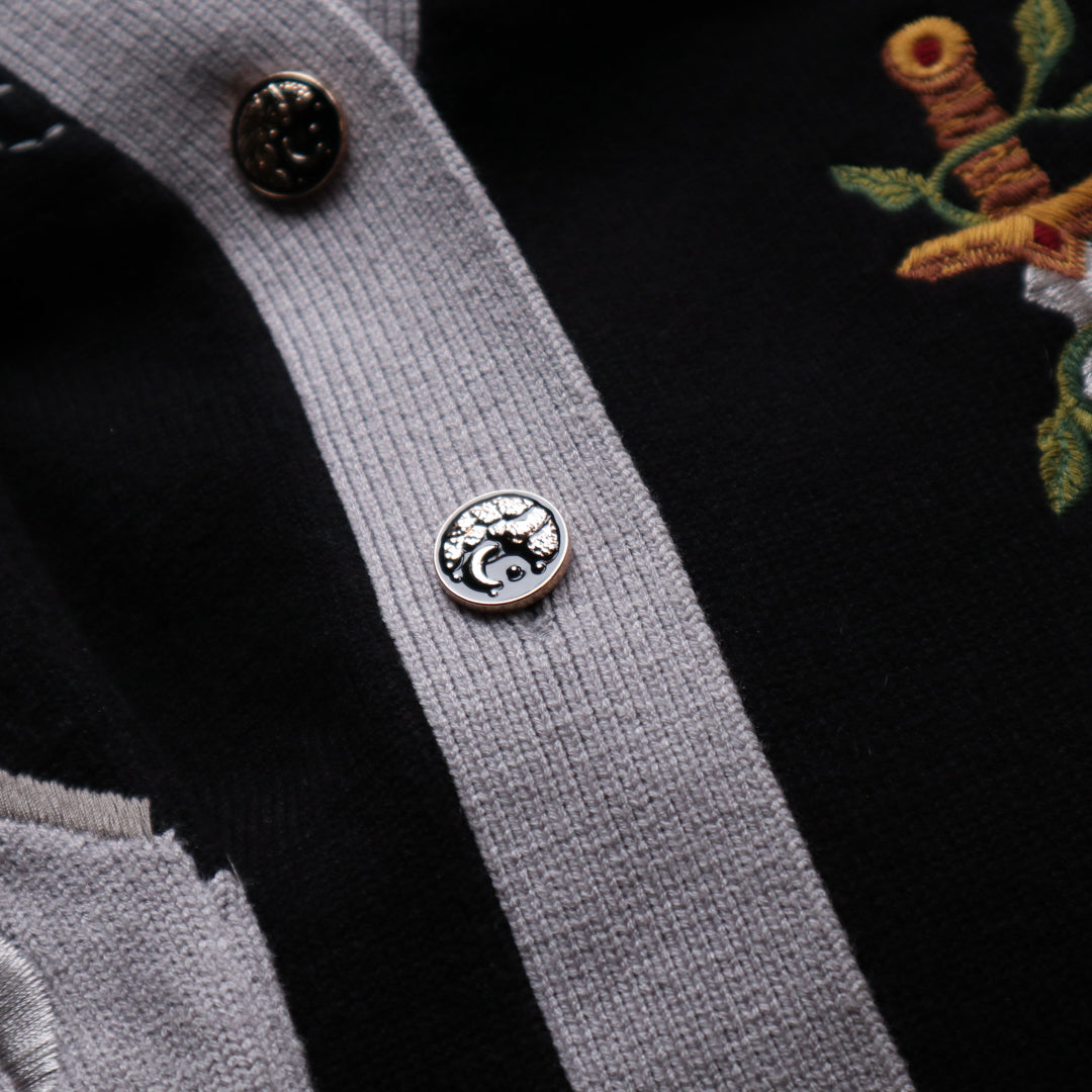 A soft button-up black and silver knit cardigan. With black and gold moon buttons, the design features intricate embroidery of a vine wrapped sword, chainmail, and armour. Evoking a whimsical and fantasy-inspired look.