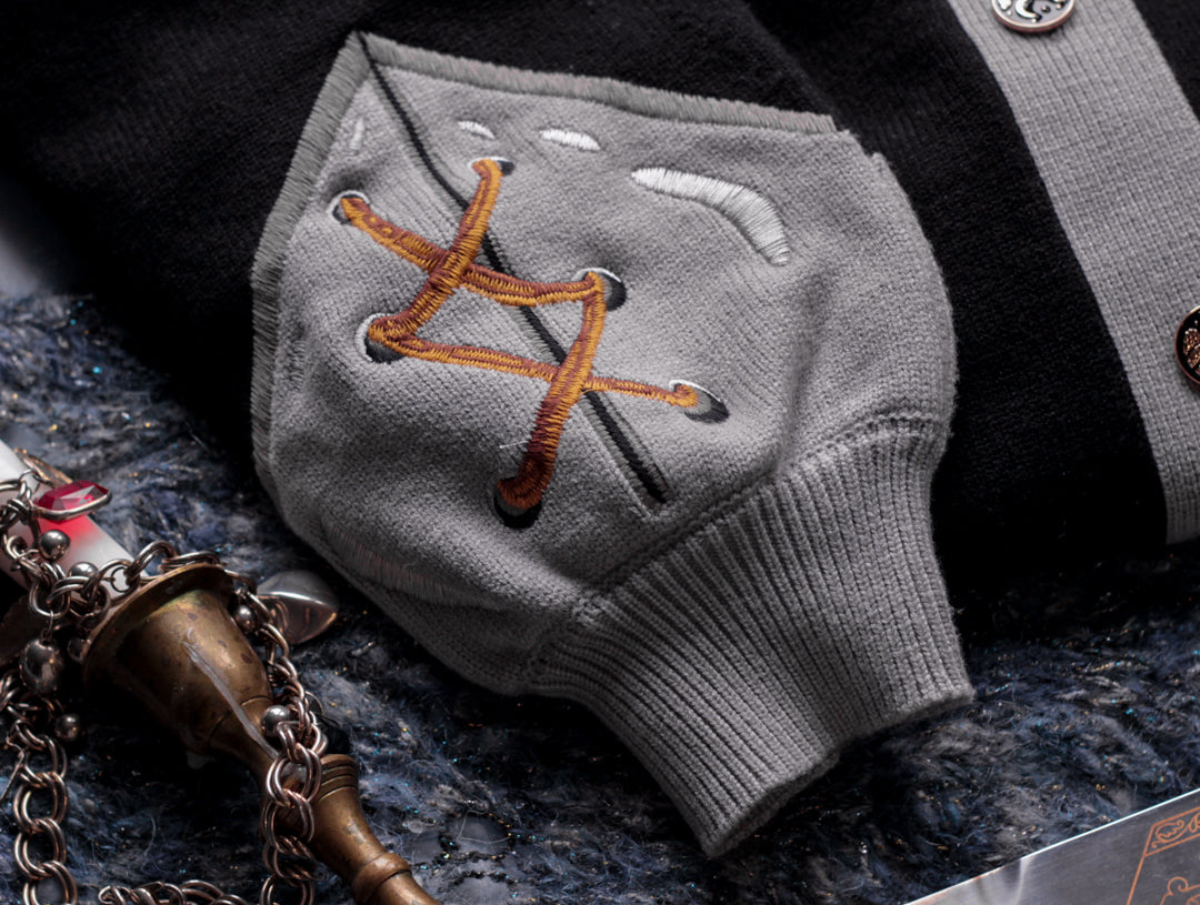 A soft button-up black and silver knit cardigan. With black and gold moon buttons, the design features intricate embroidery of a vine wrapped sword, chainmail, and armour. Evoking a whimsical and fantasy-inspired look.