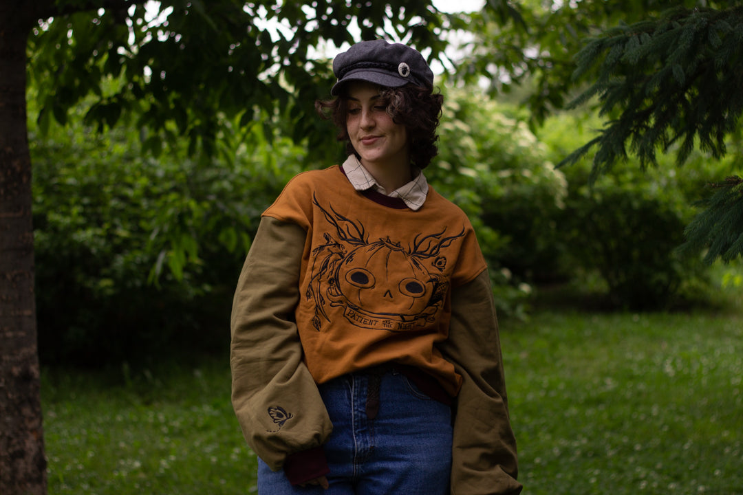 Cozy, oversized, puff-sleeved, color-blocked, cotton crewneck sweater in pumpkin-orange, olive, and burgundy. The sweater features an intricately embroidered design of a pumpkin head, branches, and other autumnal elements.