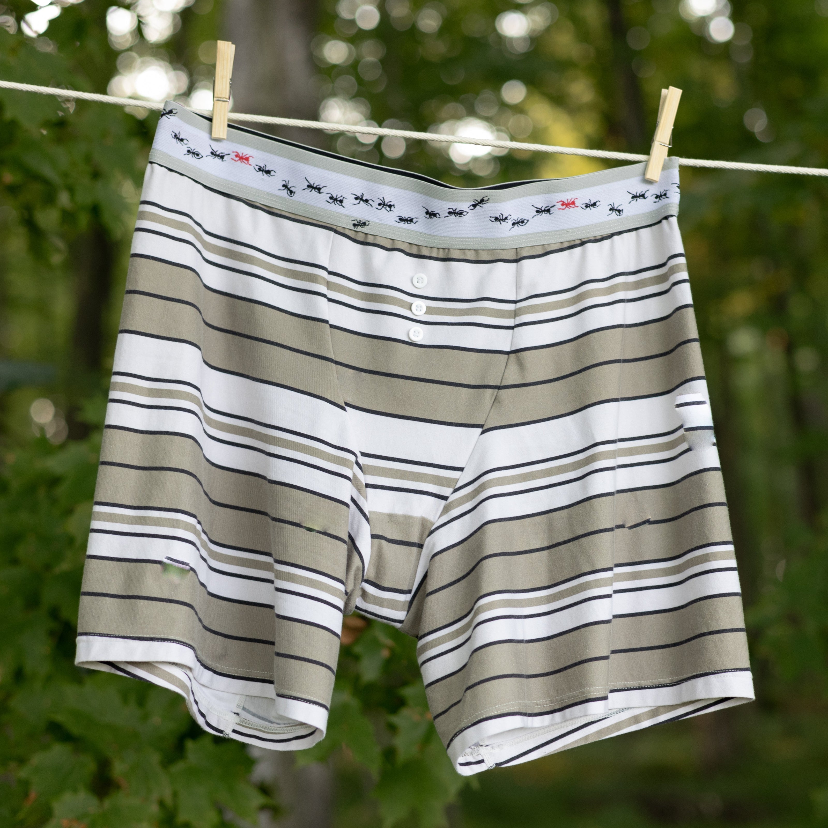 Knock Thrice Knoxers // white, black, and light olive green, striped cotton, fitted boxers. The boxers are mid-high rise,  and have a grey spandex waistband with black and red ants 
