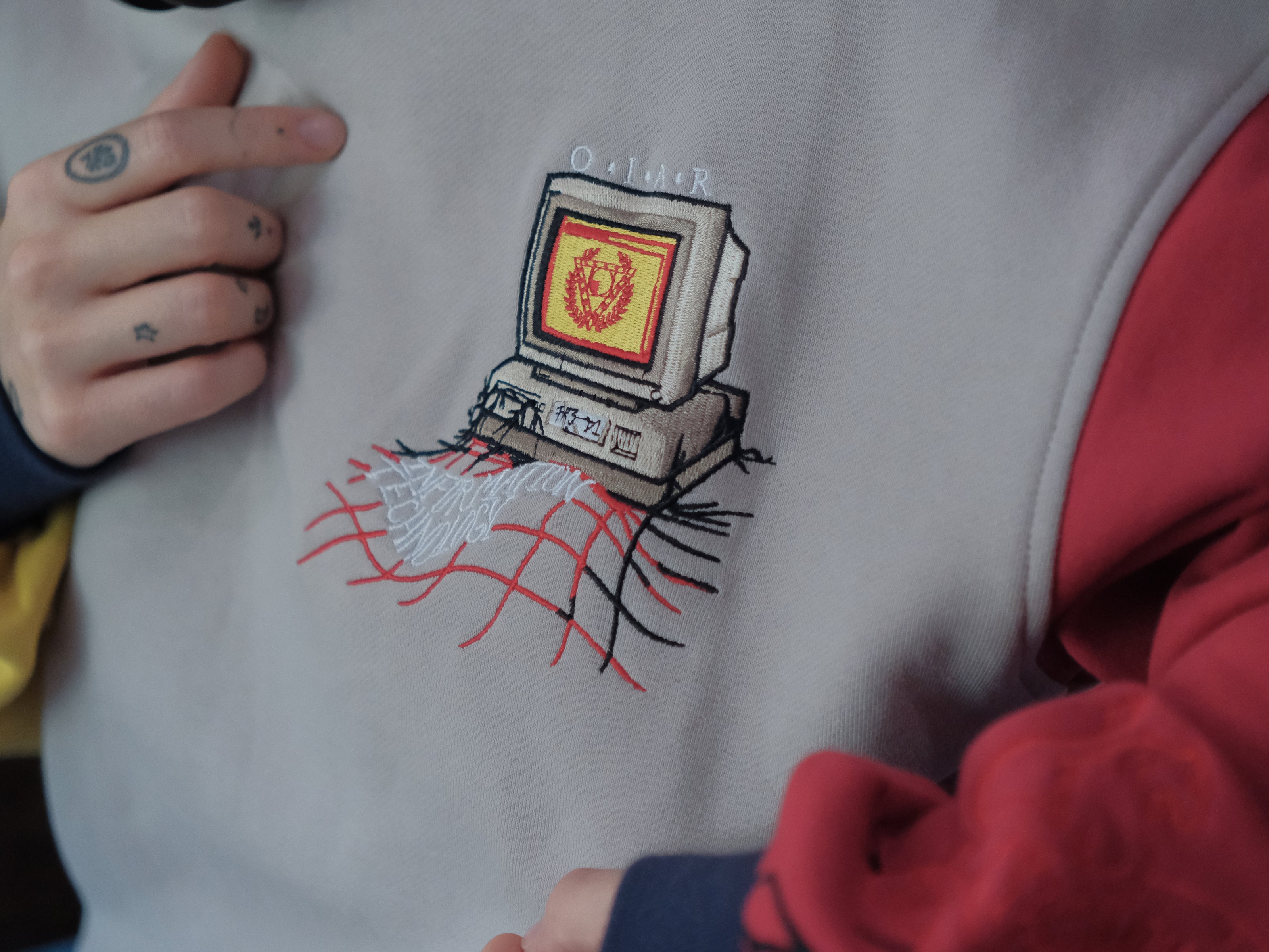 Magnus Protocol, I.T department, cotton jersey crewneck, in beige, with red and yellow colour blocked sleeves. The sweater features vaporwave computer embroidered details, and reads â€œProperty of C. Becherâ€.