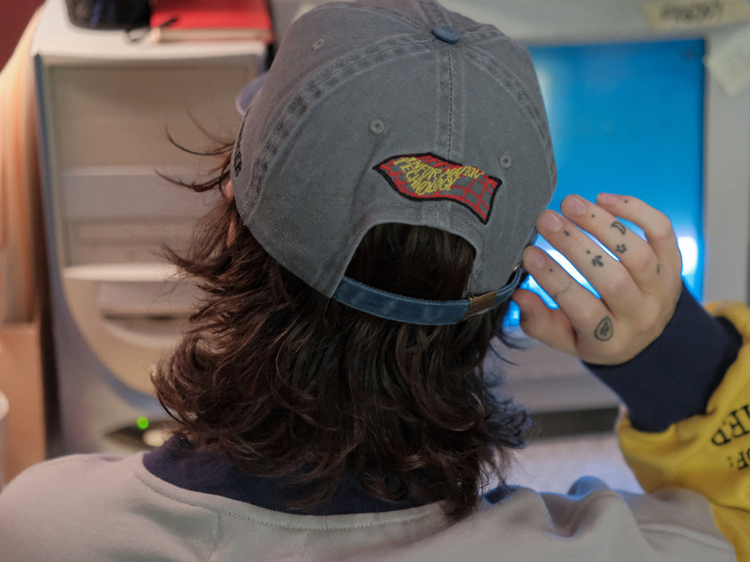 Knock Thrice x Rusty Quill, 100% cotton I.T Department Dad Cap in blue and grey. The hat features an embroidered design of a corrupted computer and glitched OIAR logo, and an adjustable fit.