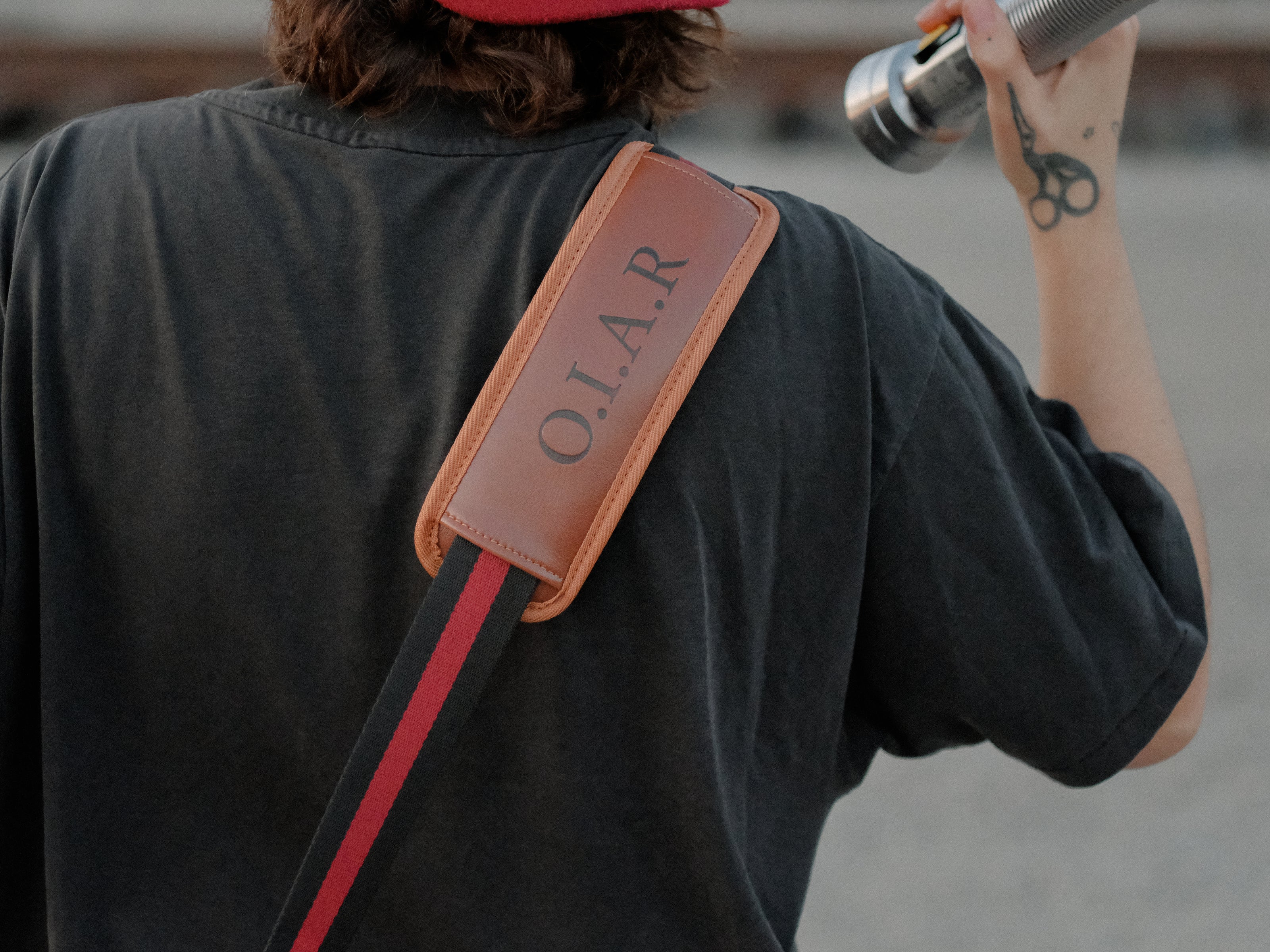 Knock Thrice x Rusty Quill canvas satchel with leather straps, plaid side panels, and an embroidered crest design. The bag is lined in plaid and includes a padded laptop pocket, adjustable cross-body strap, and magnetic closure.