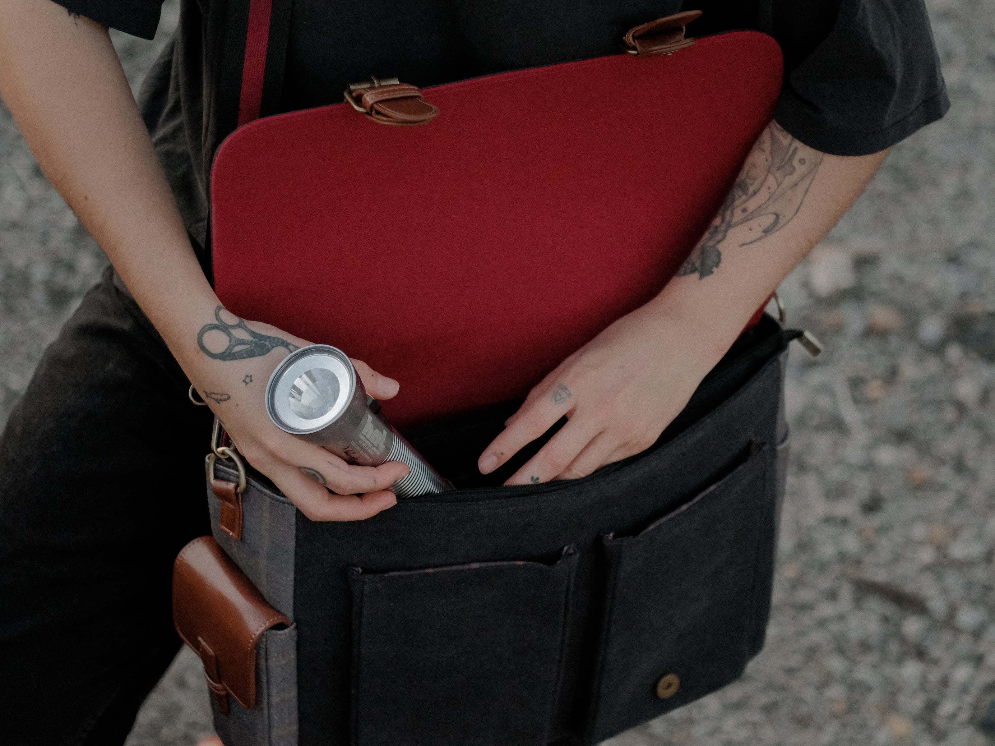 Knock Thrice x Rusty Quill canvas satchel with leather straps, plaid side panels, and an embroidered crest design. The bag is lined in plaid and includes a padded laptop pocket, adjustable cross-body strap, and magnetic closure.