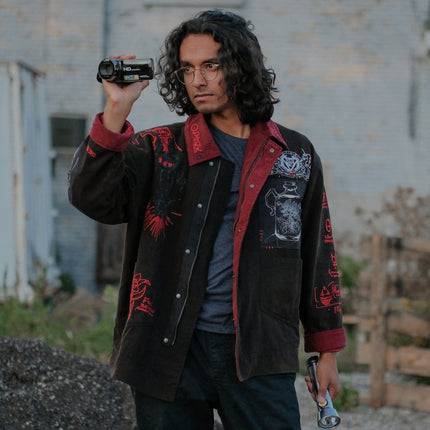 Knock Thrice x Rusty Quill, black fall/spring button-up cotton jacket, with a red corduroy lining. The jacket features both embroidered and patchwork OIAR themed elements, in red, white, and black.