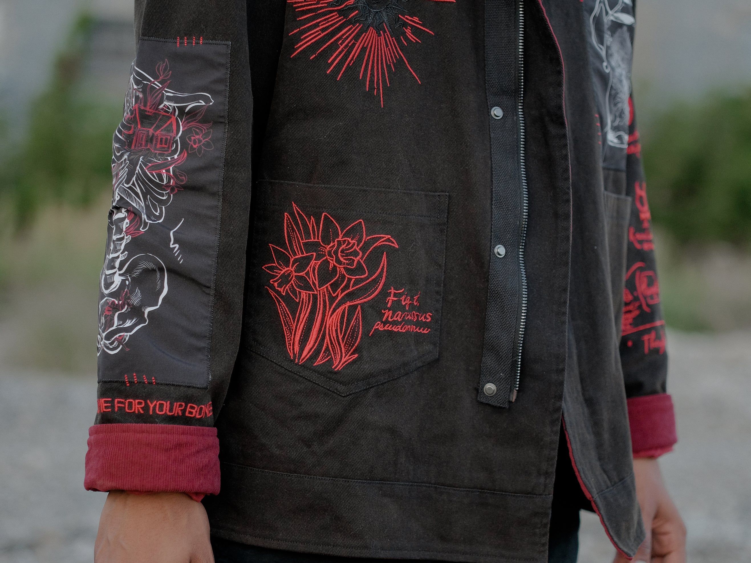 Knock Thrice x Rusty Quill, black fall/spring button-up cotton jacket, with a red corduroy lining. The jacket features both embroidered and patchwork OIAR themed elements, in red, white, and black.