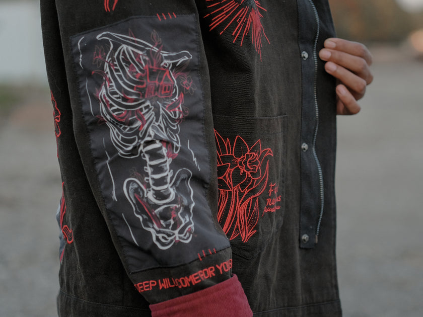 Knock Thrice x Rusty Quill, black fall/spring button-up cotton jacket, with a red corduroy lining. The jacket features both embroidered and patchwork OIAR themed elements, in red, white, and black.
