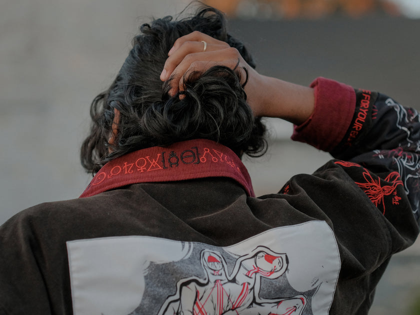 Knock Thrice x Rusty Quill, black fall/spring button-up cotton jacket, with a red corduroy lining. The jacket features both embroidered and patchwork OIAR themed elements, in red, white, and black.