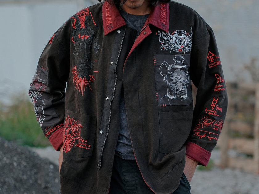 Knock Thrice x Rusty Quill, black fall/spring button-up cotton jacket, with a red corduroy lining. The jacket features both embroidered and patchwork OIAR themed elements, in red, white, and black.