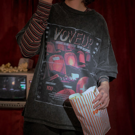 Knock Thrice x Rusty Quill, oversized, stone-washed cotton tee, with a graphic design titled 'Voyeur,' showcasing an eerie movie theatre with red seats, bold text reading 'Needs to be seen to be believed,' and film-inspired details.
