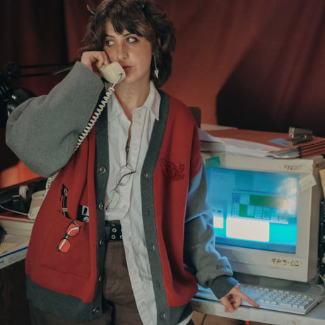 Magnus Protocol, oversized, knit-cardigan, in red, black, and shades of grey. The cardigan features embroidered details of reading glasses, fountain pen, OIAR crest, and reads â€œOffice of Incident Assessment & Responseâ€.