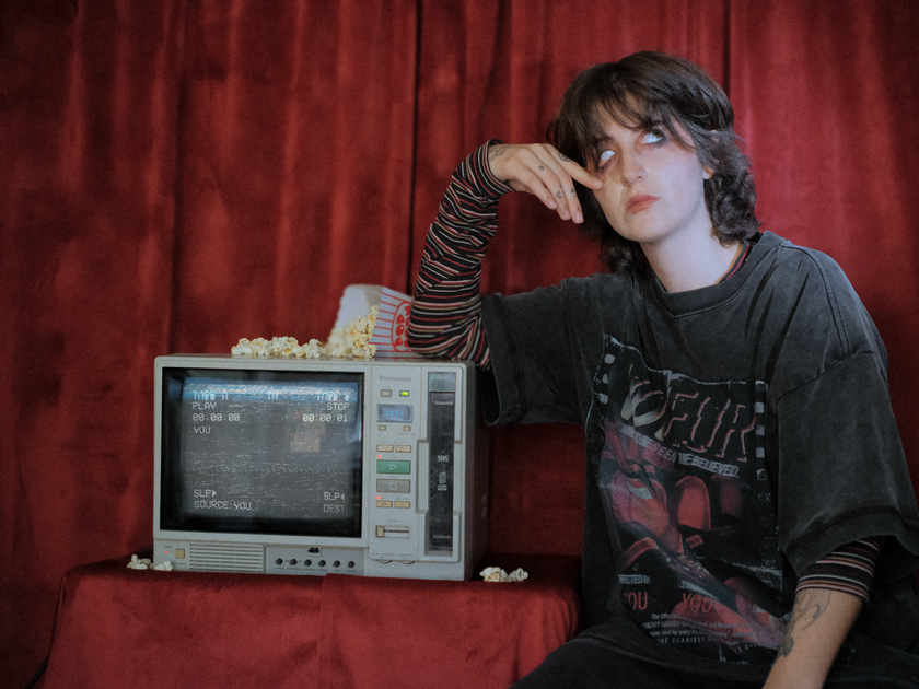 Knock Thrice x Rusty Quill, oversized, stone-washed cotton tee, with a graphic design titled 'Voyeur,' showcasing an eerie movie theatre with red seats, bold text reading 'Needs to be seen to be believed,' and film-inspired details.