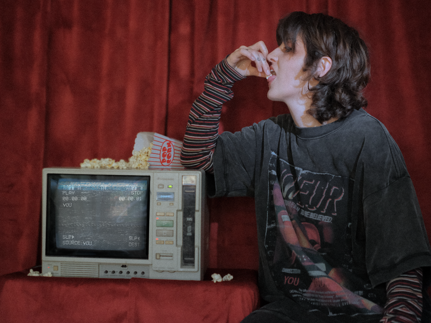 Knock Thrice x Rusty Quill, oversized, stone-washed cotton tee, with a graphic design titled 'Voyeur,' showcasing an eerie movie theatre with red seats, bold text reading 'Needs to be seen to be believed,' and film-inspired details.