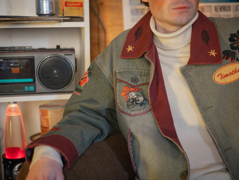 Knock Thrice x Rusty Quill, black fall/spring button-up cotton jacket. The jacket features both embroidered and patchwork OIAR themed elements, in red, and green.