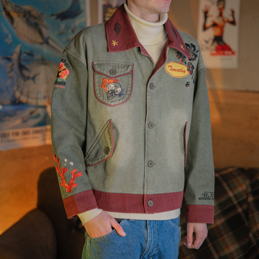 Knock Thrice x Rusty Quill, black fall/spring button-up cotton jacket. The jacket features both embroidered and patchwork OIAR themed elements, in red, and green.