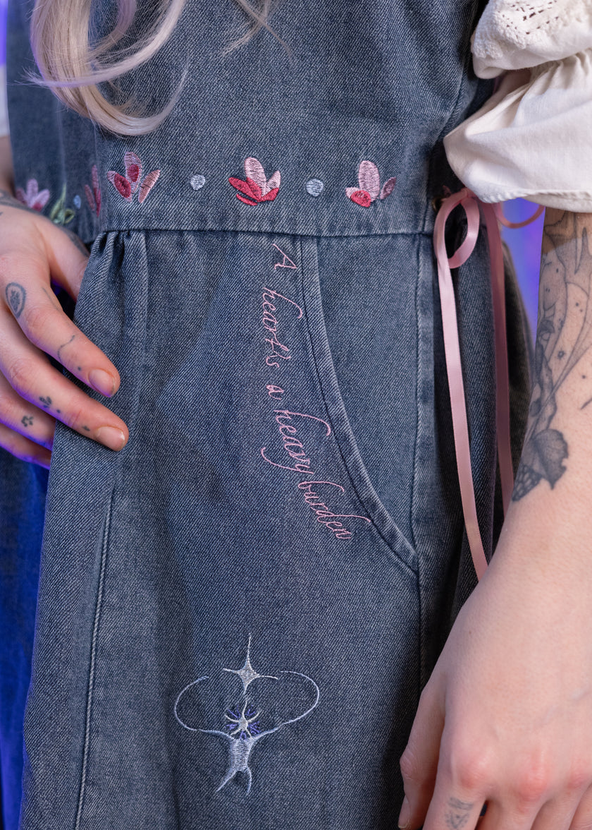 Denim dress with embroidered designs and text, worn by a person.