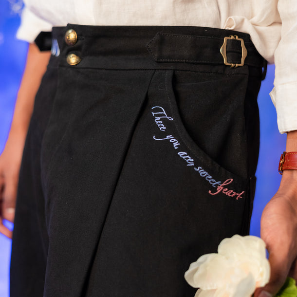 100% cotton cuffed trousers featuring side adjustments, elastic back band,  large front and back pockets, gold hardware, and colourful embroidered details.