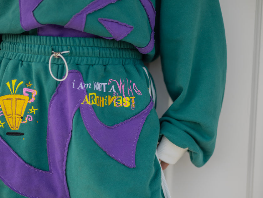 Magnus Archives x Knock Thrice “I’m a What” long shorts in green and purple, 100% cotton graphic shorts with embroidered details