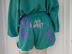 Magnus Archives x Knock Thrice “I’m a What” long shorts in green and purple, 100% cotton graphic shorts with embroidered details