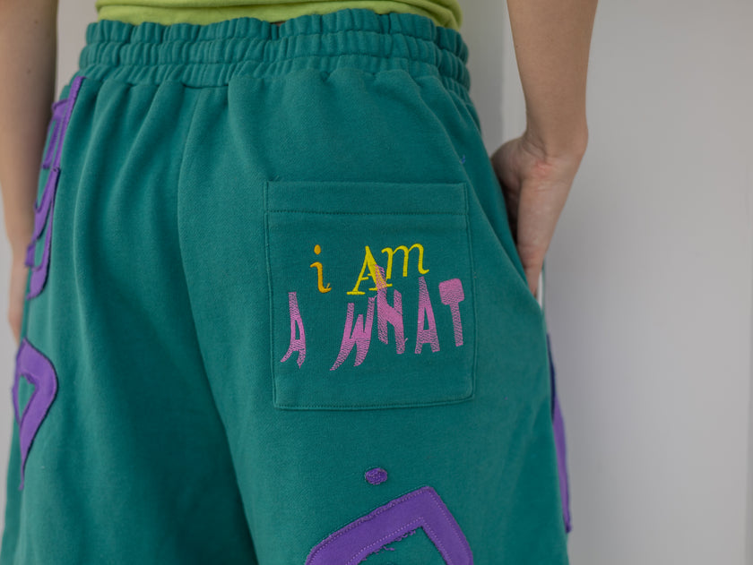 Magnus Archives x Knock Thrice “I’m a What” long shorts in green and purple, 100% cotton graphic shorts with embroidered details