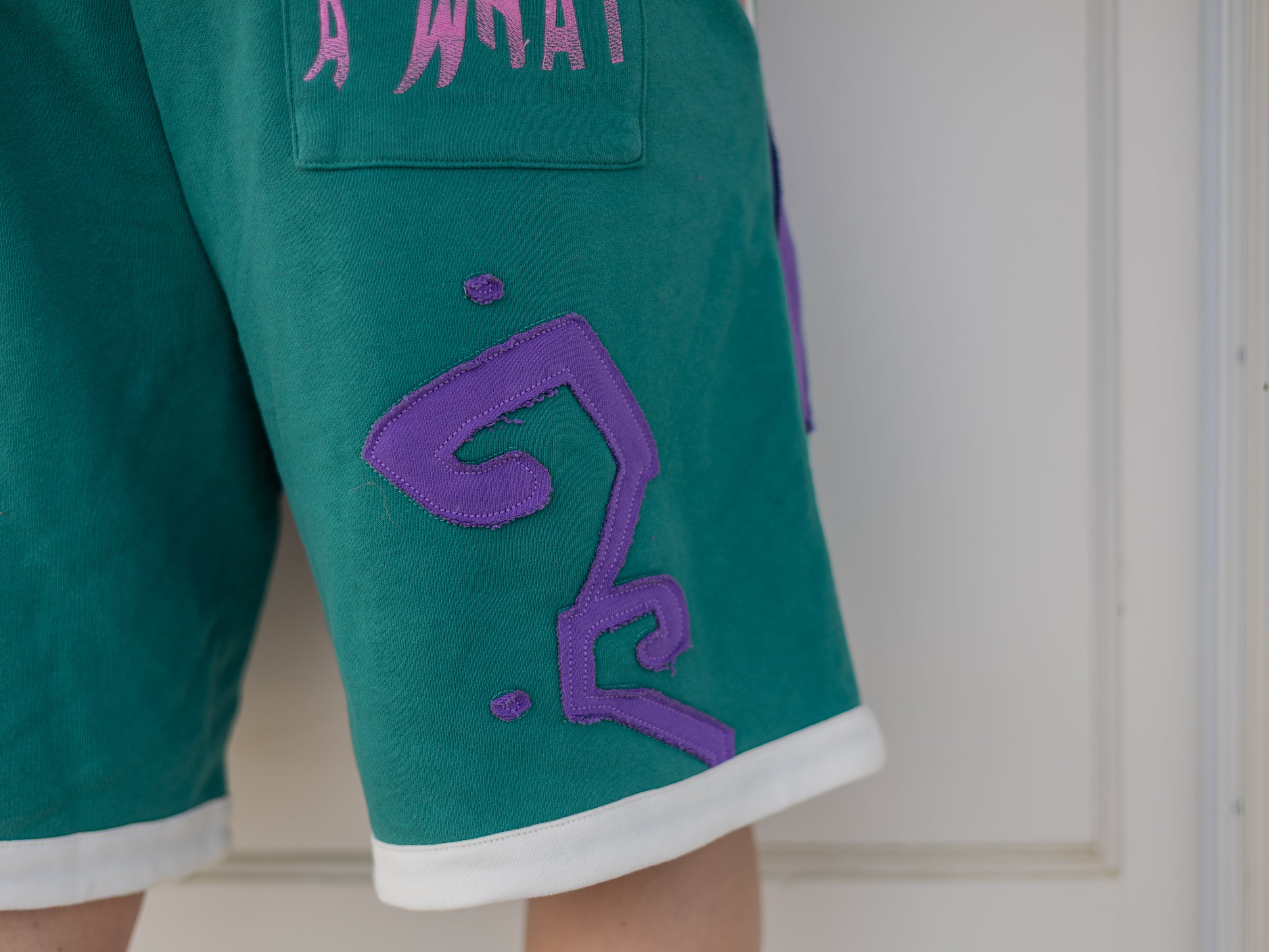 Magnus Archives x Knock Thrice “I’m a What” long shorts in green and purple, 100% cotton graphic shorts with embroidered details