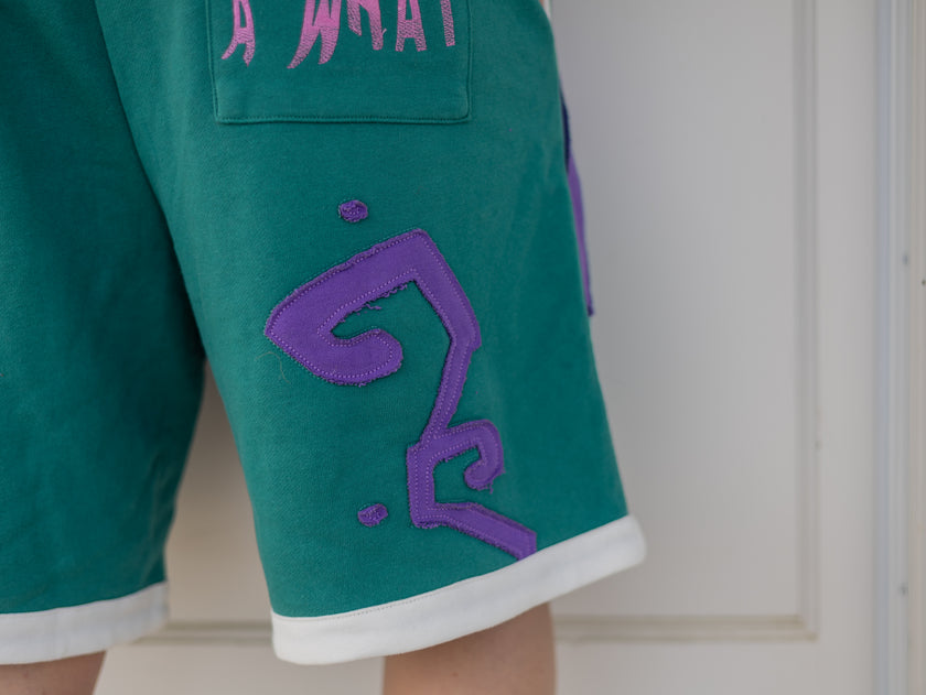 Magnus Archives x Knock Thrice “I’m a What” long shorts in green and purple, 100% cotton graphic shorts with embroidered details