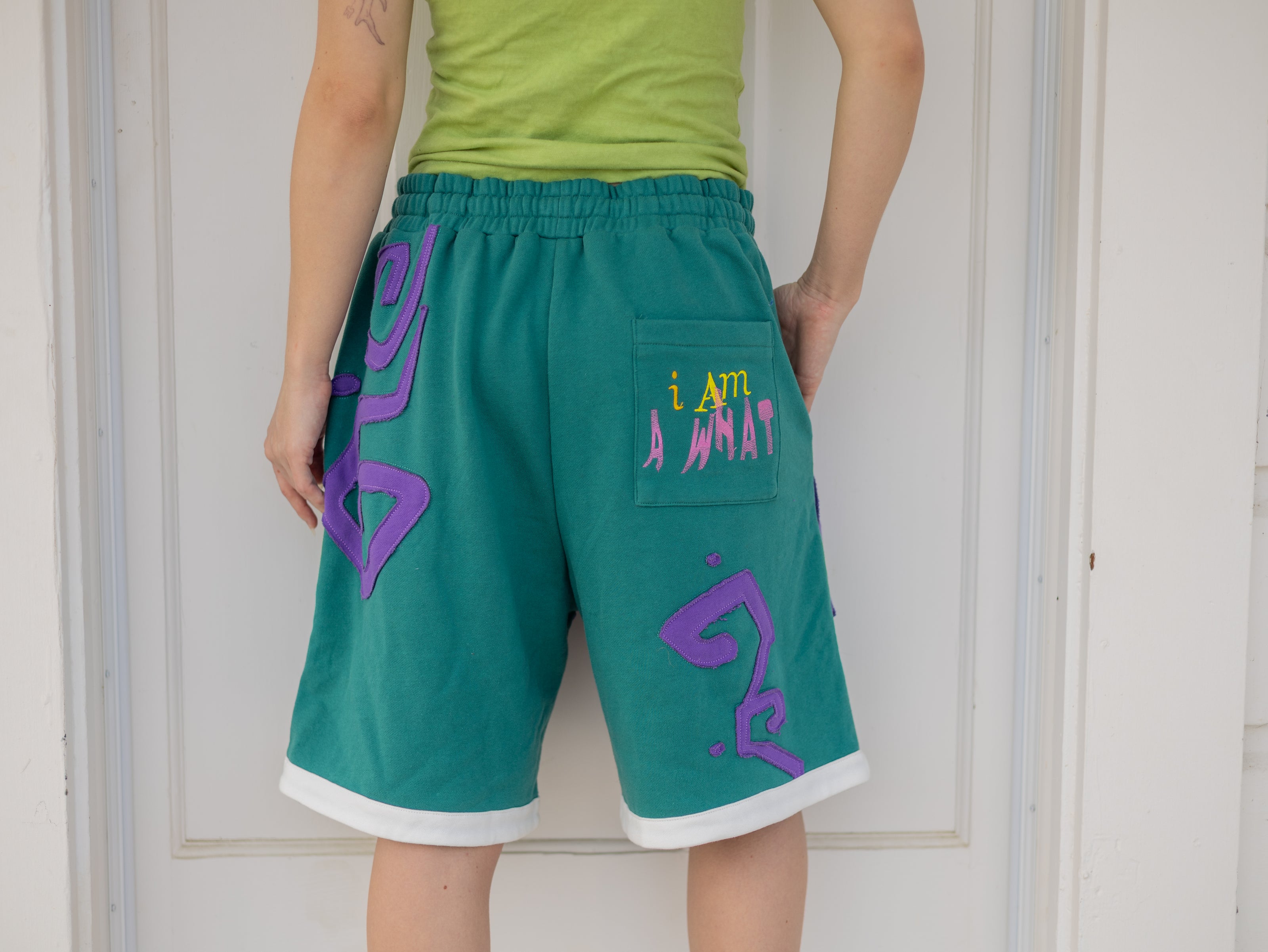 Magnus Archives x Knock Thrice “I’m a What” long shorts in green and purple, 100% cotton graphic shorts with embroidered details