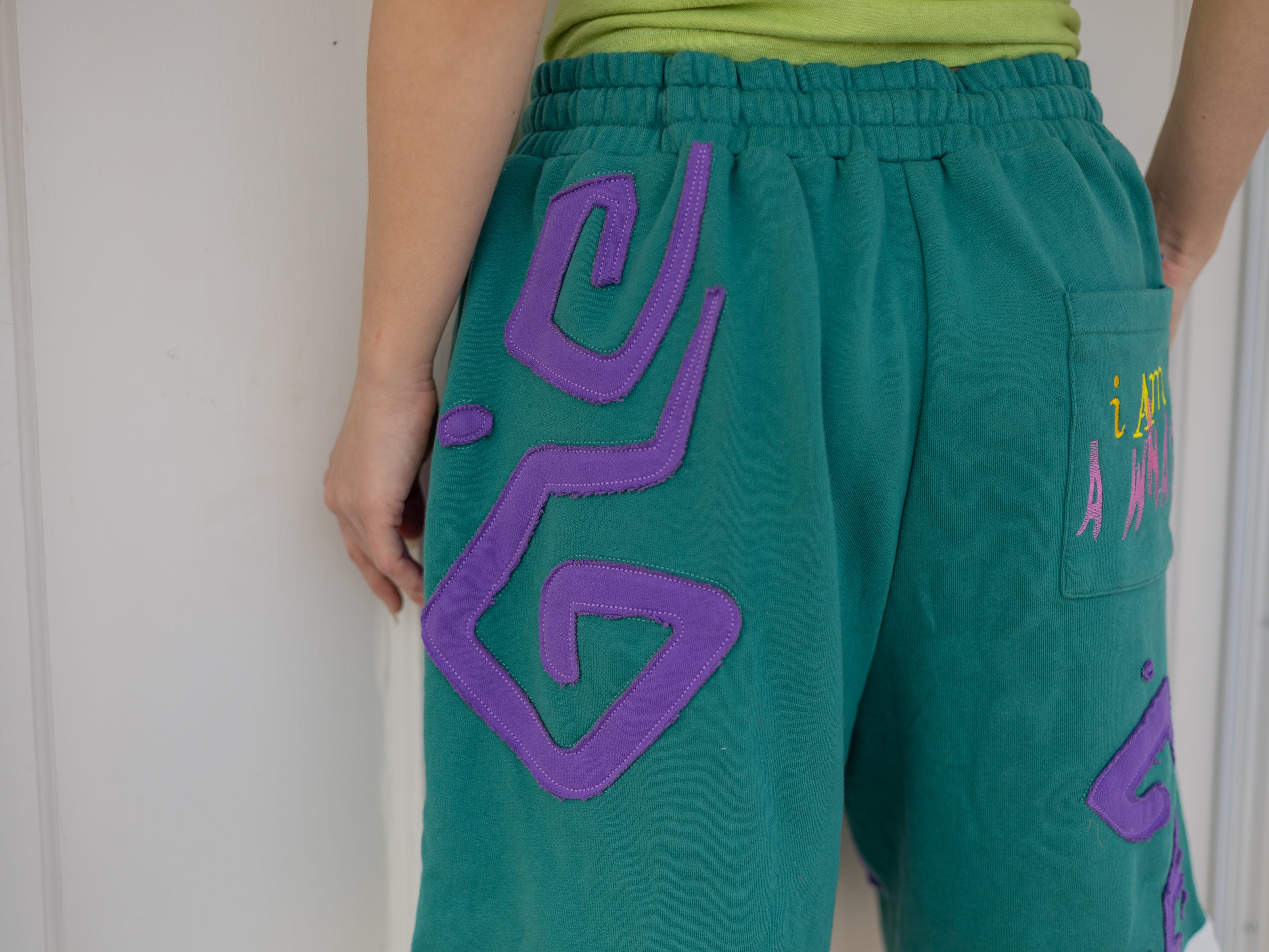 Magnus Archives x Knock Thrice “I’m a What” long shorts in green and purple, 100% cotton graphic shorts with embroidered details