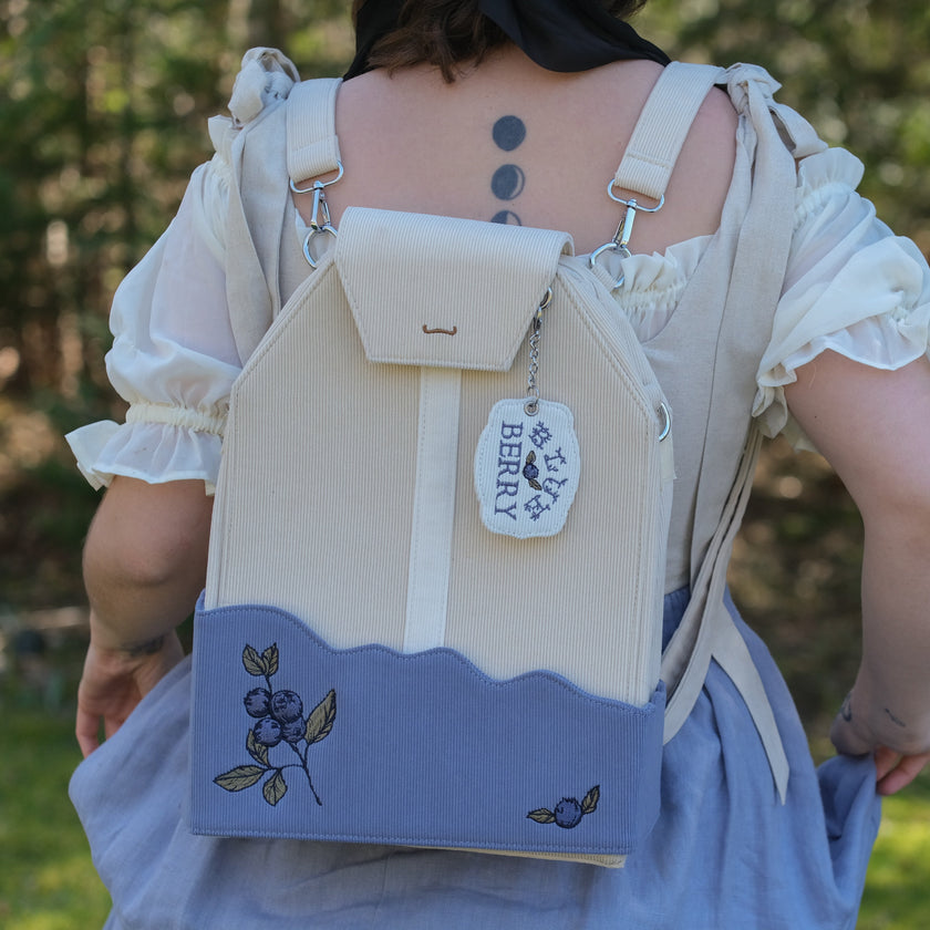 Person wearing a beige and blue backpack with 'BERRY' tag outdoors