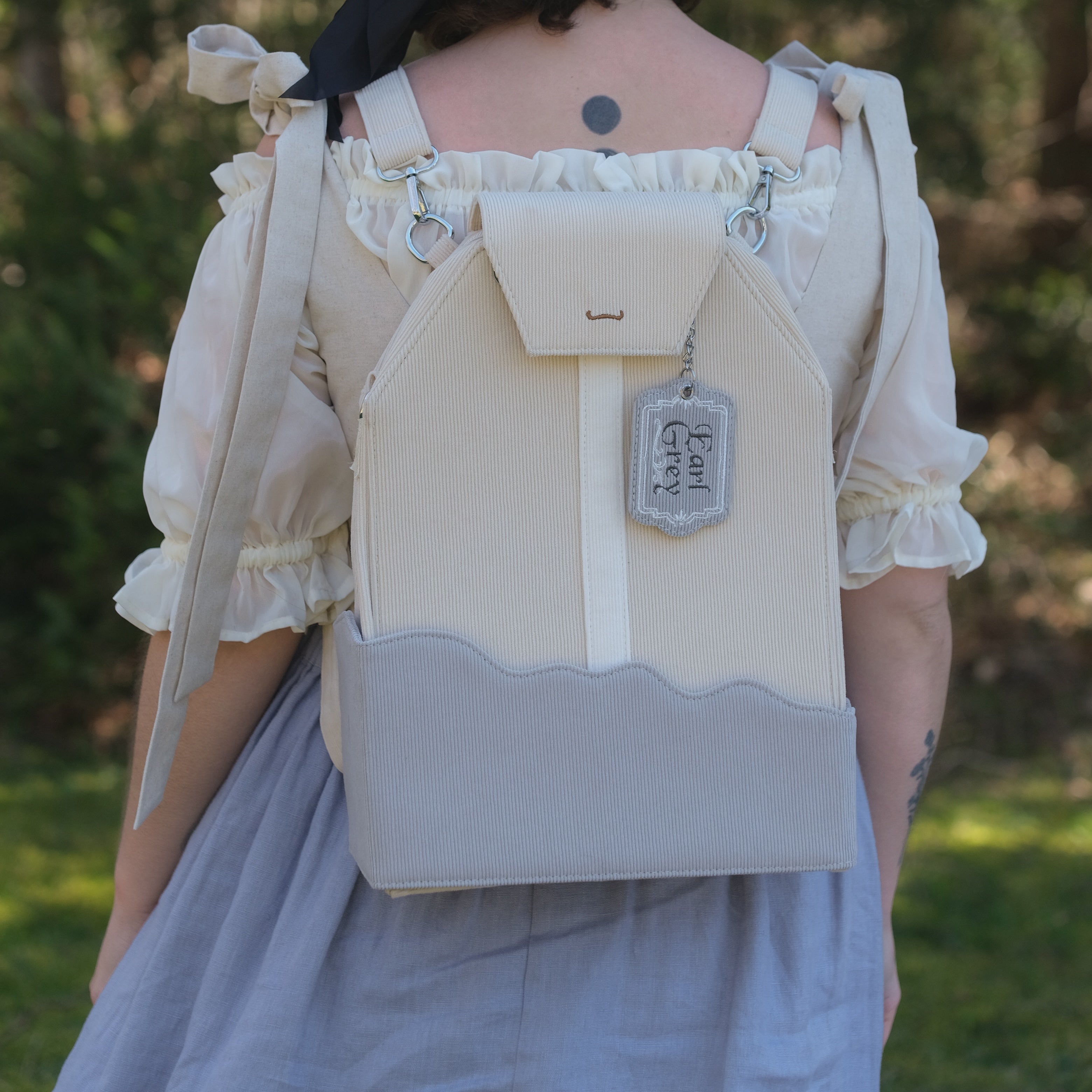 Person wearing a beige and gray backpack with decorative elements outdoors.