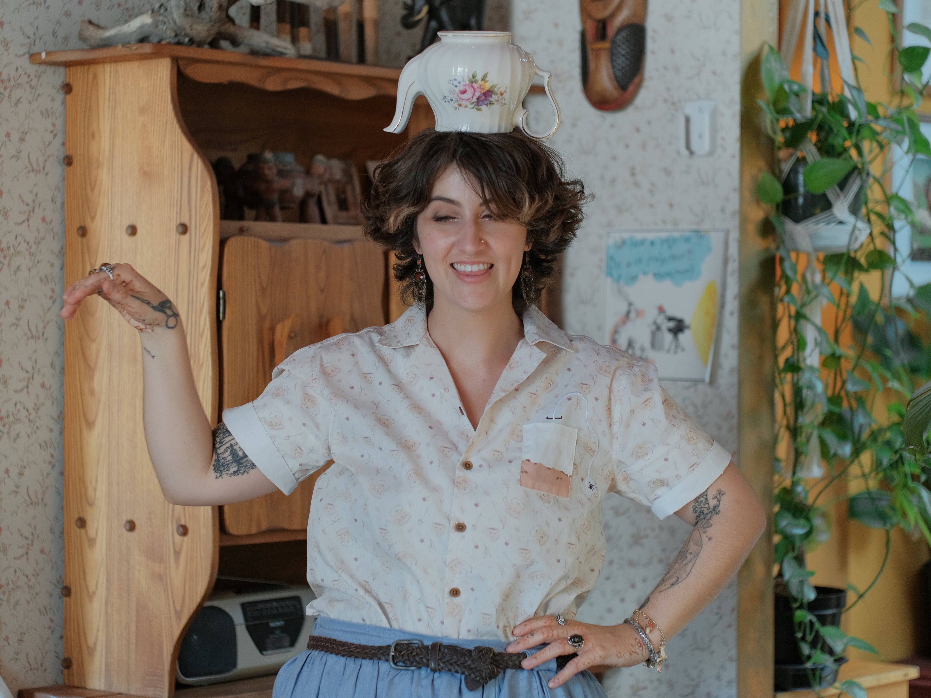 A warm ivory/cream colour short-sleeve button up t-shirt printed with a whimsical pattern of classic chubby teapots and matching cups, autumnal oak leaves, tea bags, spoons and sugar cubes. The shirt has a pyramid tea bag pocket, as well as a relaxed fit and rolled cuffs.