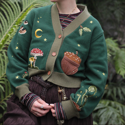 A 100% cotton, forest-green, cropped knit cardigan. The design features intricate woodland embroidery, evoking a whimsical and fantasy-inspired look.